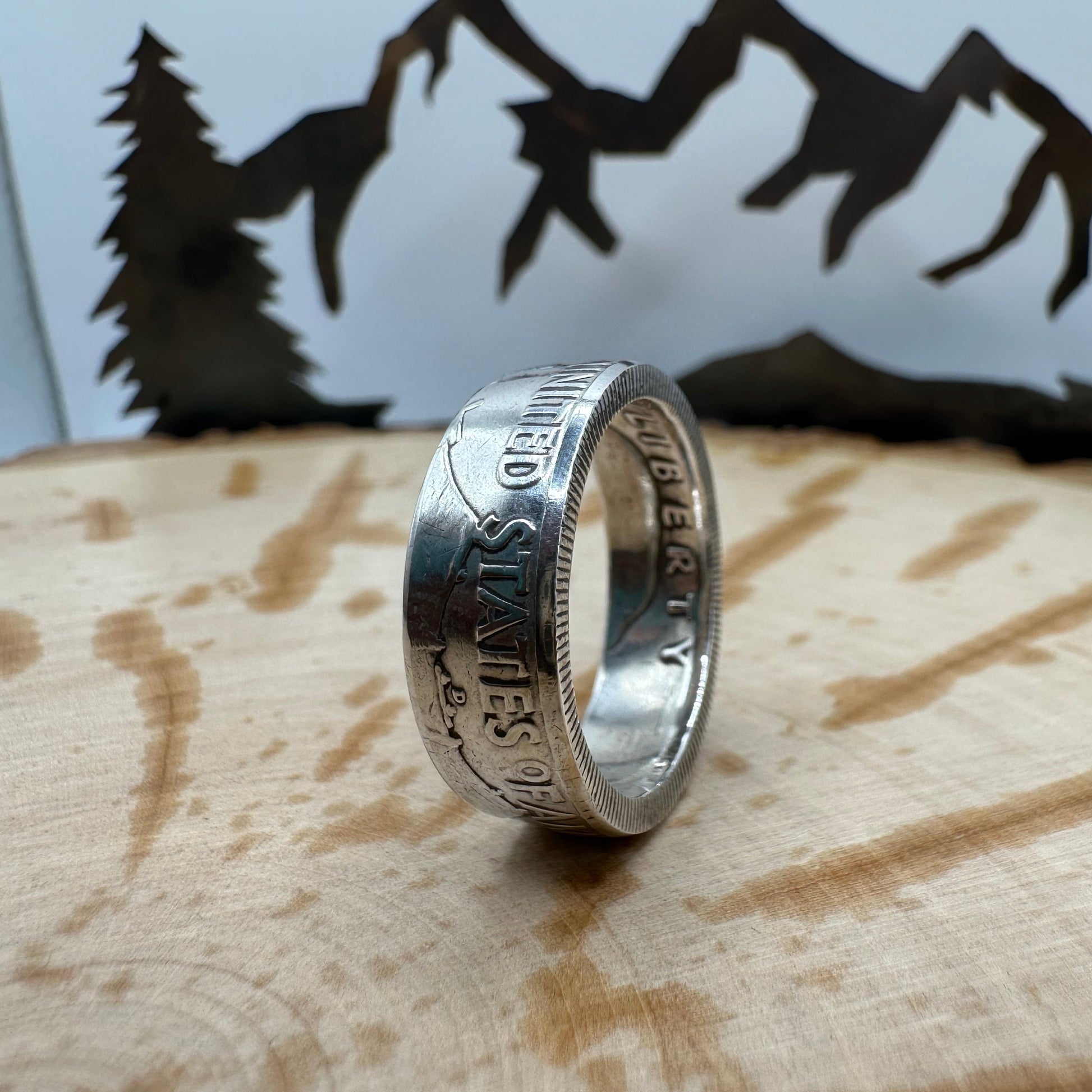 Ben Franklin Half Dollar Silver Coin Ring on a light wood round with a metal mountain and tree background. - Mountainstruck Coin Jewelry