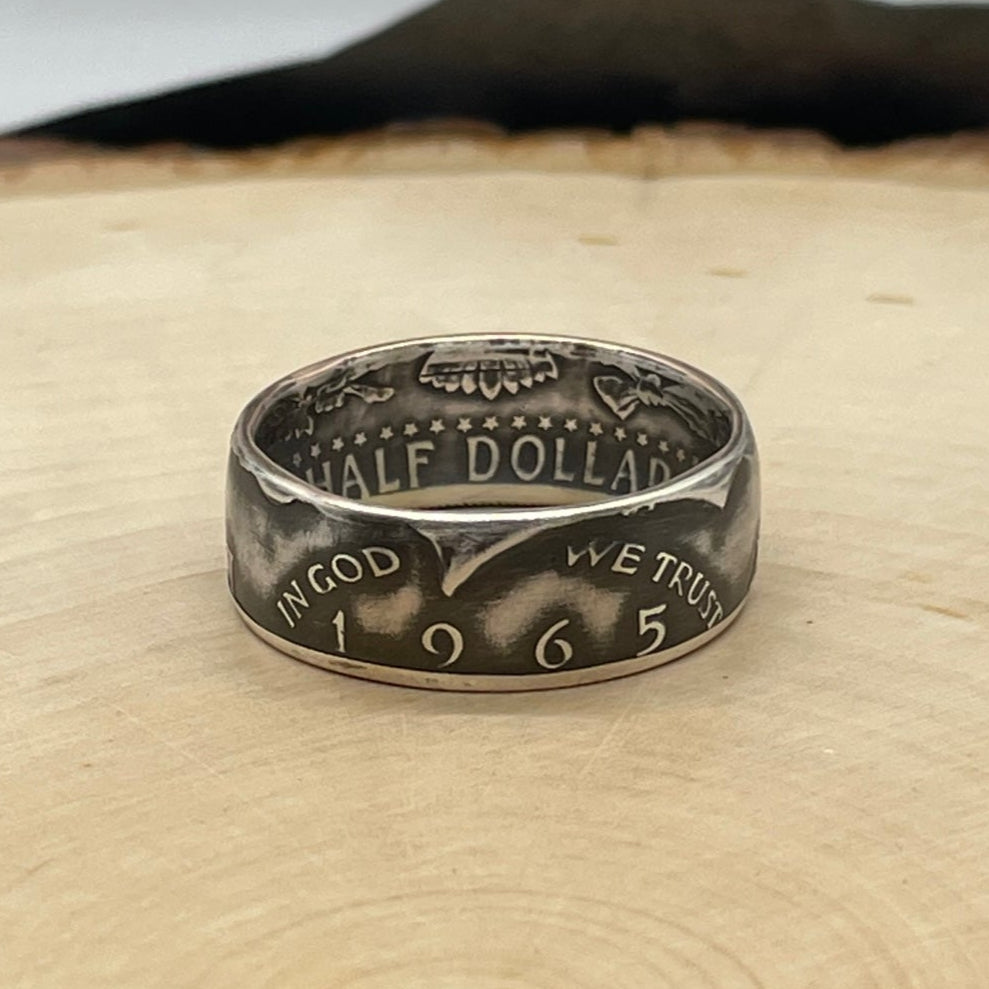 JFK Silver Half Dollar Coin Ring (front) on a light wood round with mountain outline in background. - Mountainstruck Coin Jewelry