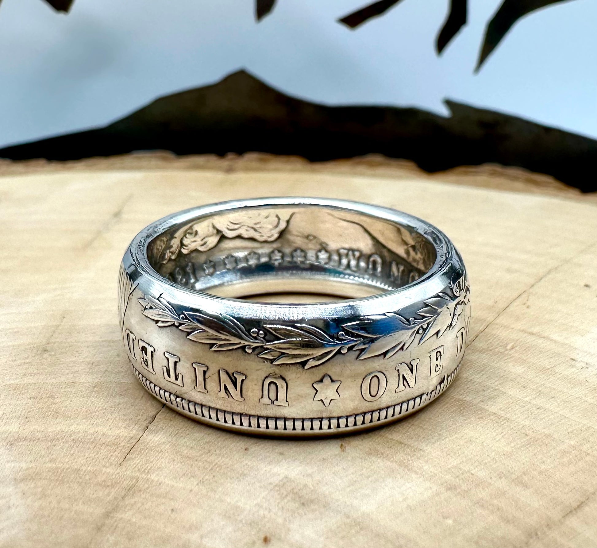 Morgan Dollar Silver Coin Ring on a light wood round with a metal mountain background. - Mountainstruck Coin Jewelry