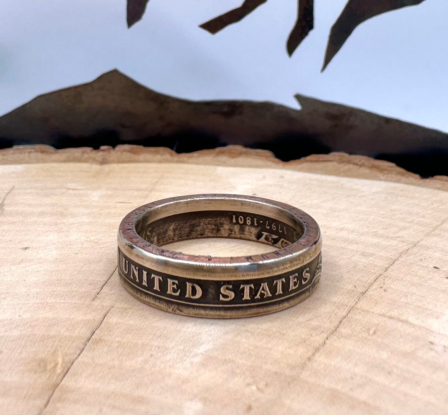 Presidential Dollar Coin Ring (Reverse) patina on a light wood round with a metal mountain background. - Mountainstruck Coin Jewelry