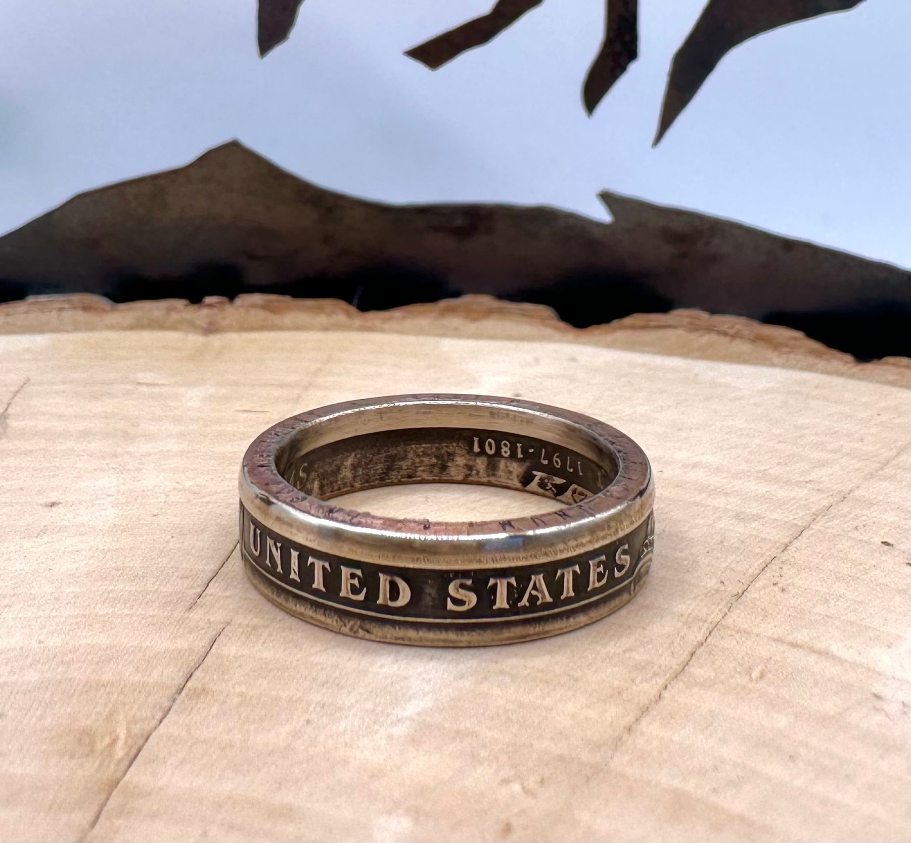Presidential Dollar Coin Ring (Reverse) patina on a light wood round with a metal mountain background. - Mountainstruck Coin Jewelry