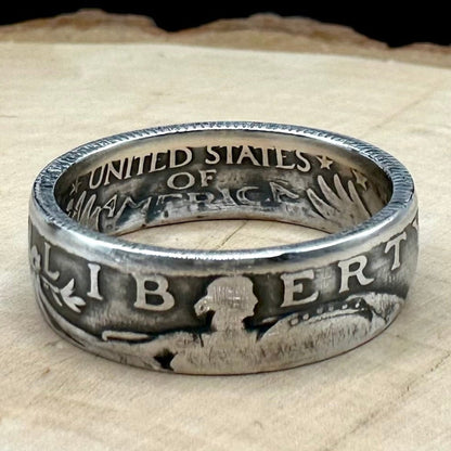 U.S. Standing Liberty Quarter Silver Coin Ring a light wood round with a metal mountain background. - Mountainstruck Coin Jewelry