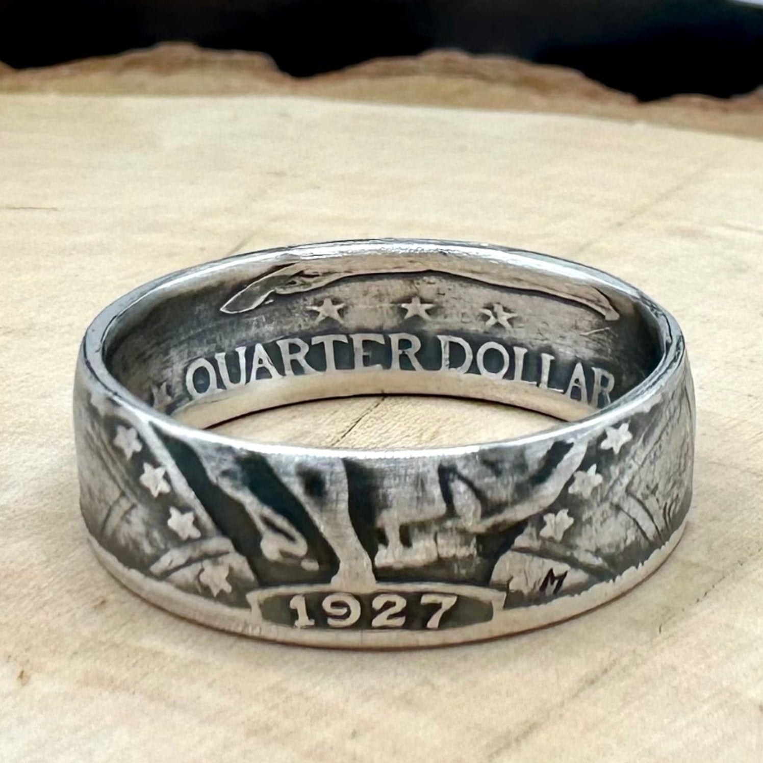 U.S. Standing Liberty Quarter Silver Coin Ring a light wood round with a metal mountain background. - Mountainstruck Coin Jewelry