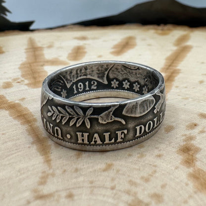 U.S. Barber Half Dollar Silver Coin Ring (reverse) on a light wood round with a metal mountain background. - Mountainstruck Coin Jewelry
