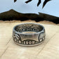 U.S. Barber Silver Half Dollar Coin Ring (front) on a light wood round with metal mountains in the background. - Mountainstruck Coin Jewelry