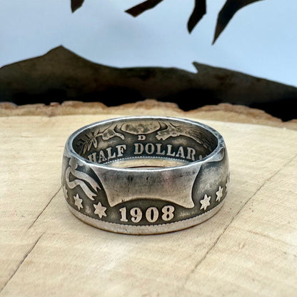 U.S. Barber Silver Half Dollar Coin Ring (front) on a light wood round with metal mountains in the background. - Mountainstruck Coin Jewelry