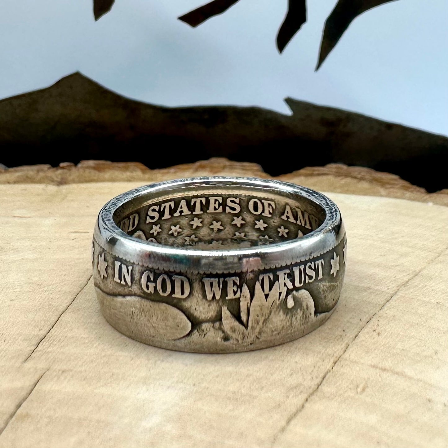U.S. Barber Silver Half Dollar Coin Ring (front) on a light wood round with metal mountains in the background. - Mountainstruck Coin Jewelry