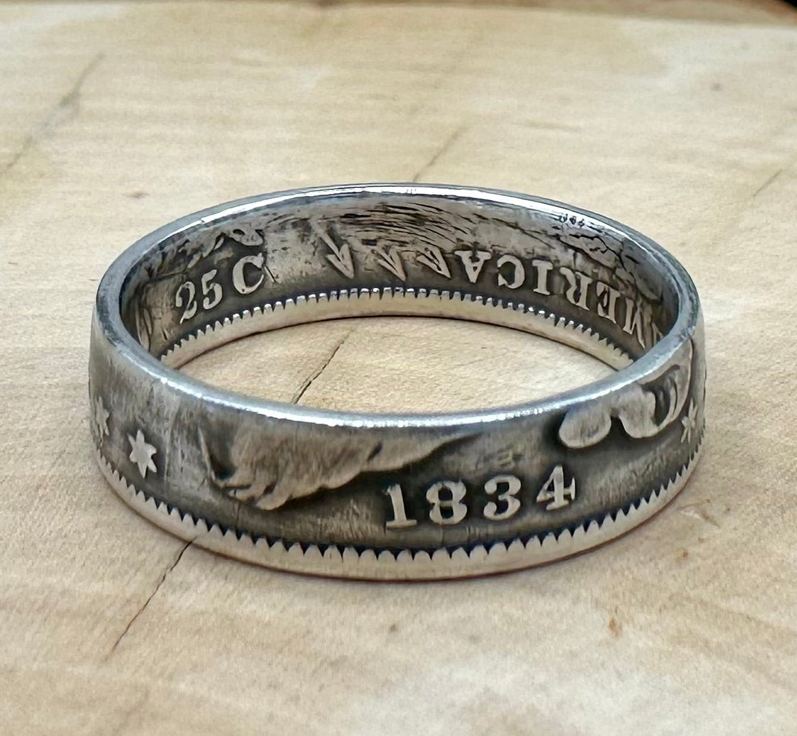 U.S. Capped Bust Liberty Quarter Silver Coin Ring on a light wood round with metal mountain background. - Mountainstruck Coin Jewelry