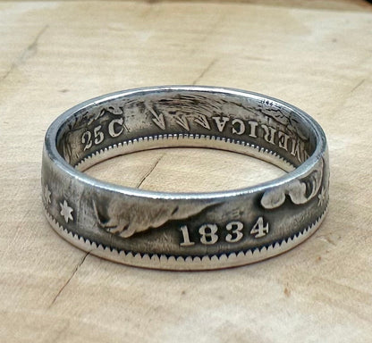 U.S. Capped Bust Liberty Quarter Silver Coin Ring on a light wood round with metal mountain background. - Mountainstruck Coin Jewelry
