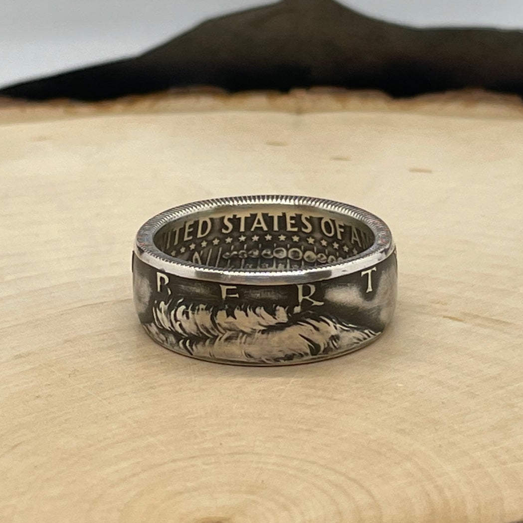 U.S. JFK Silver Half Dollar Coin Ring (front) on a light wood round with mountain outline in background. - Mountainstruck Coin Jewelry