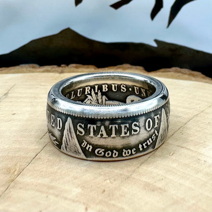 U.S. Morgan Dollar Silver Coin Ring patina size 10 on a light wood round with a metal mountain background. - Mountainstruck Coin Jewelry