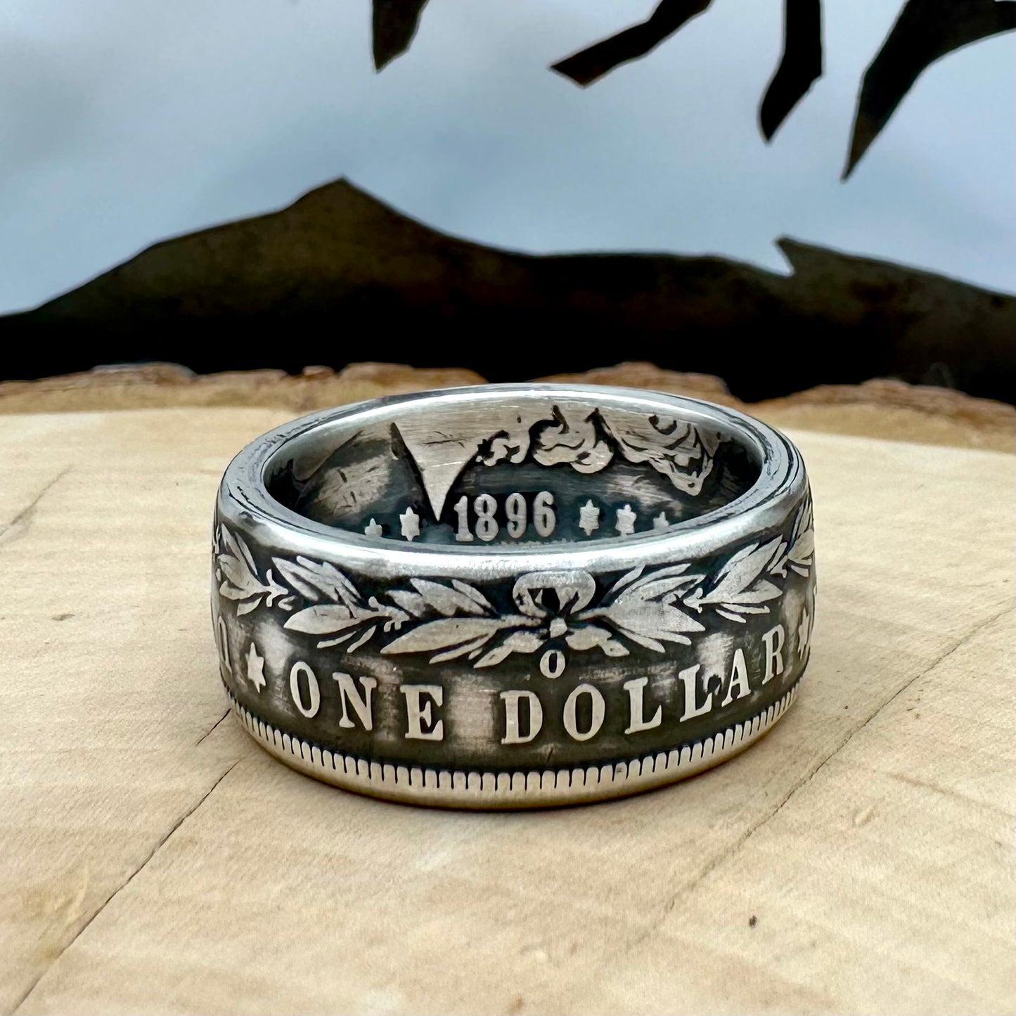 U.S. Morgan Dollar Silver Coin Ring patina size 10 on a light wood round with a metal mountain background. - Mountainstruck Coin Jewelry