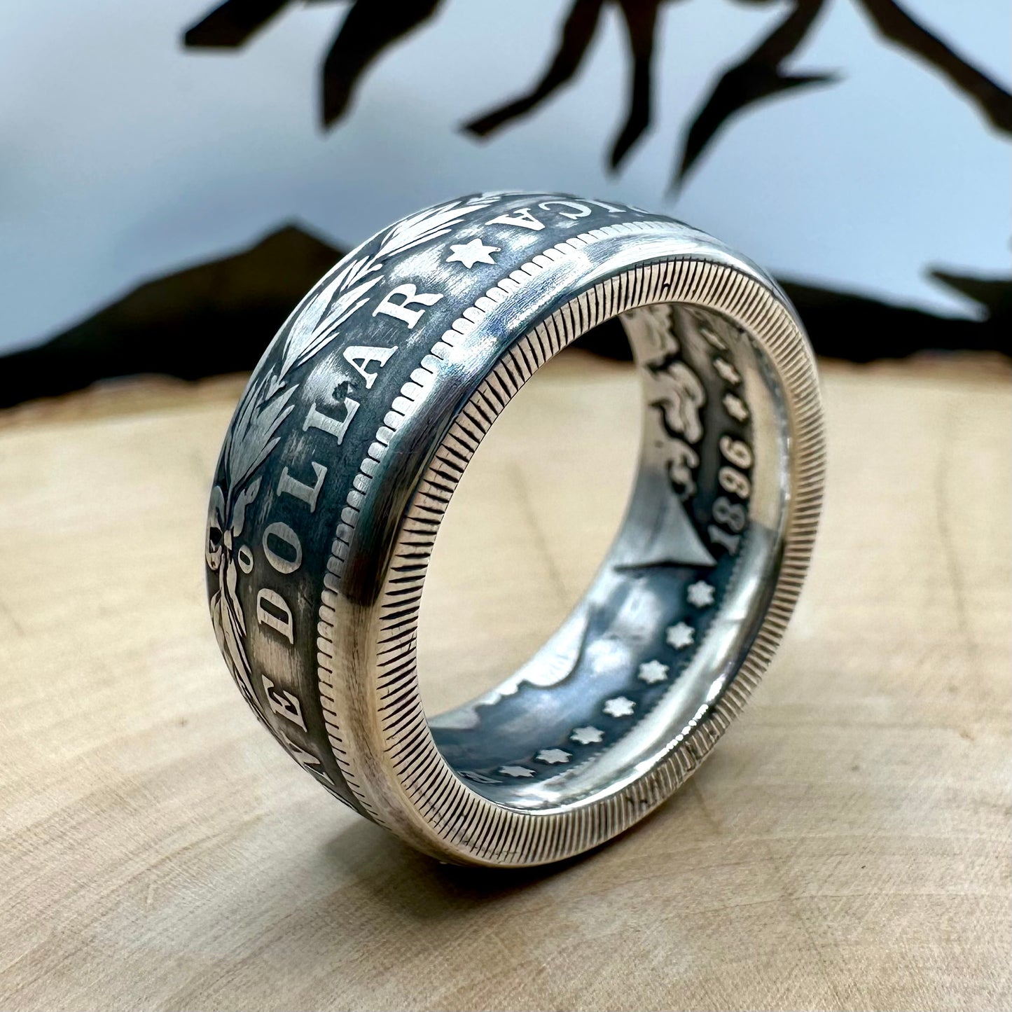 U.S. Morgan Dollar Silver Coin Ring patina size 10 on a light wood round with a metal mountain background. - Mountainstruck Coin Jewelry