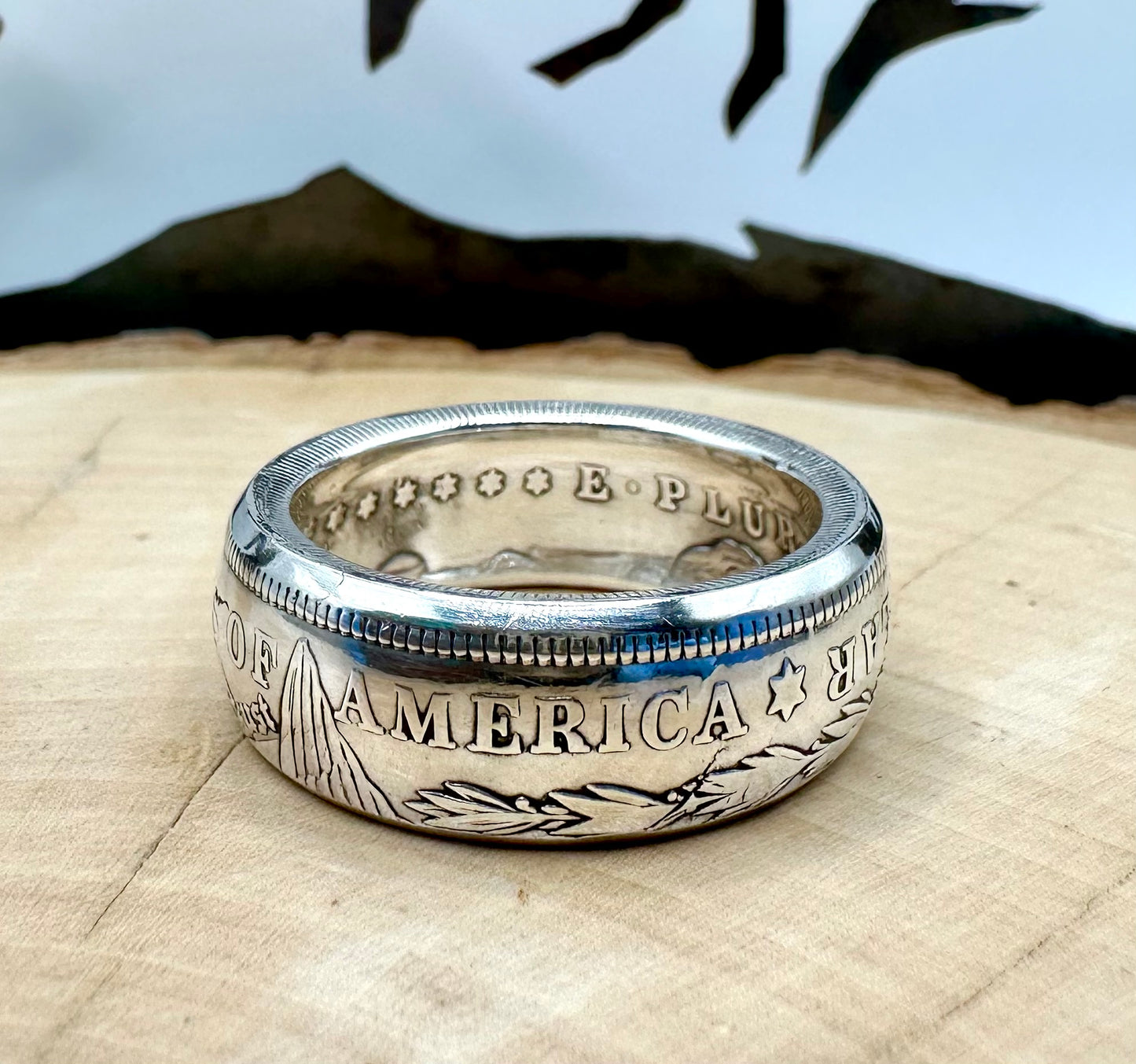 U.S. Morgan Dollar Silver Coin Ring shine on a light wood round with a metal mountain background. - Mountainstruck Coin Jewelry