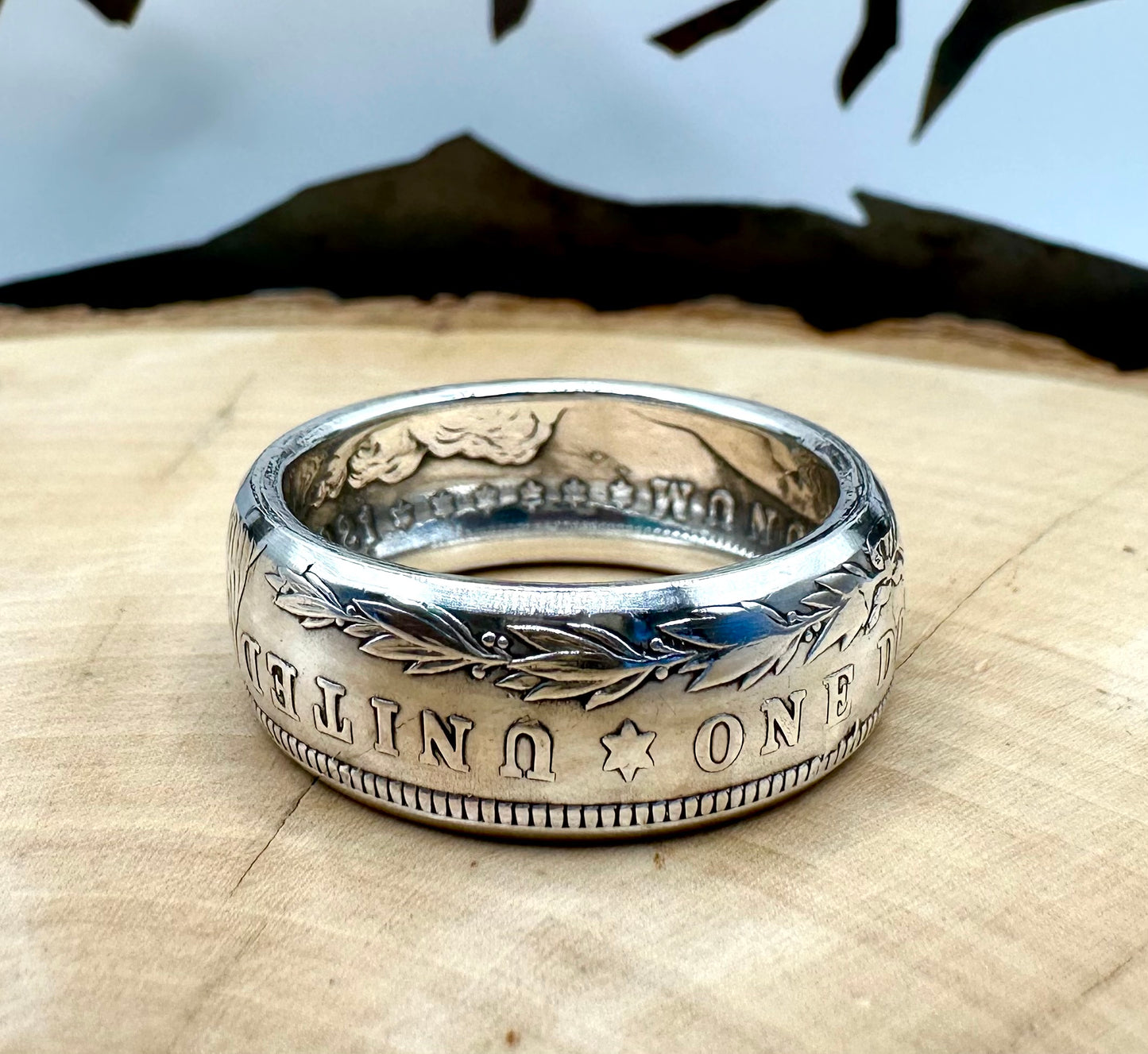 U.S. Morgan Dollar Silver Coin Ring on a light wood round with a metal mountain background. - Mountainstruck Coin Jewelry
