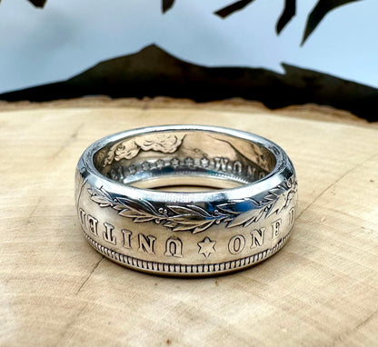 U.S. Morgan Dollar Silver Coin Ring on a light wood round with a metal mountain background. - Mountainstruck Coin Jewelry