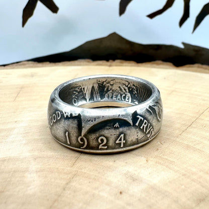 U.S. Peace Dollar Silver Coin Ring on a light wood round with a metal mountain background. - Mountainstruck Coin Jewelry