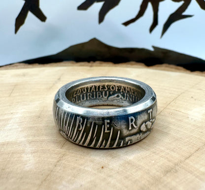 U.S. Peace Dollar Silver Coin Ring on a light wood round with a metal mountain background. - Mountainstruck Coin Jewelry