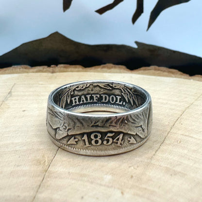  U.S. Seated Liberty Silver Half Dollar Coin Ring (patina) on a light wood round with a metal mountain background. - Mountainstruck Coin Jewelry