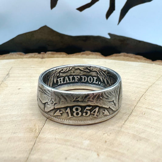  U.S. Seated Liberty Silver Half Dollar Coin Ring (patina) on a light wood round with a metal mountain background. - Mountainstruck Coin Jewelry