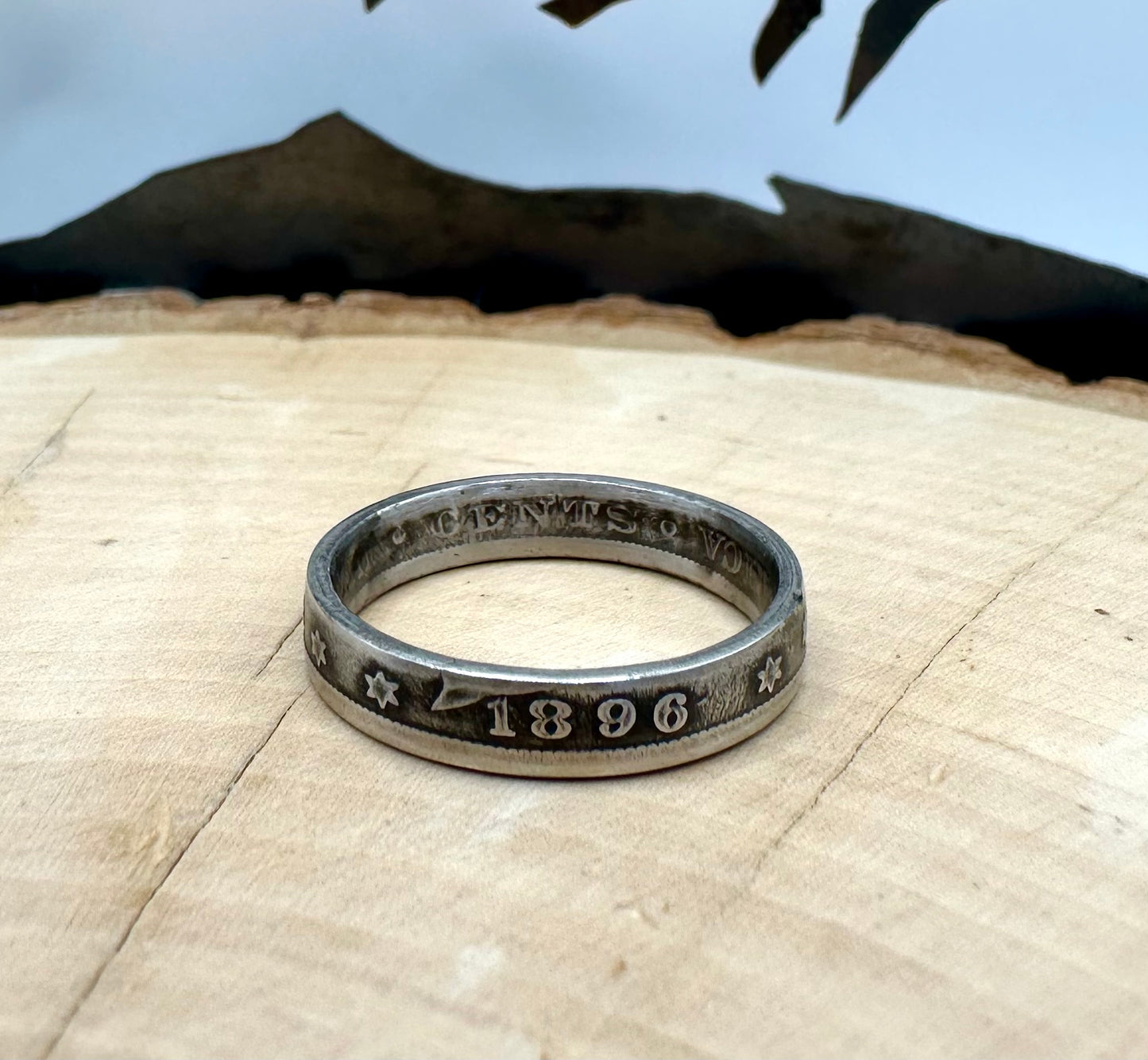 "V" Nickel Coin Ring on a light wood round with a metal mountain background. - Mountainstruck Coin Jewelry