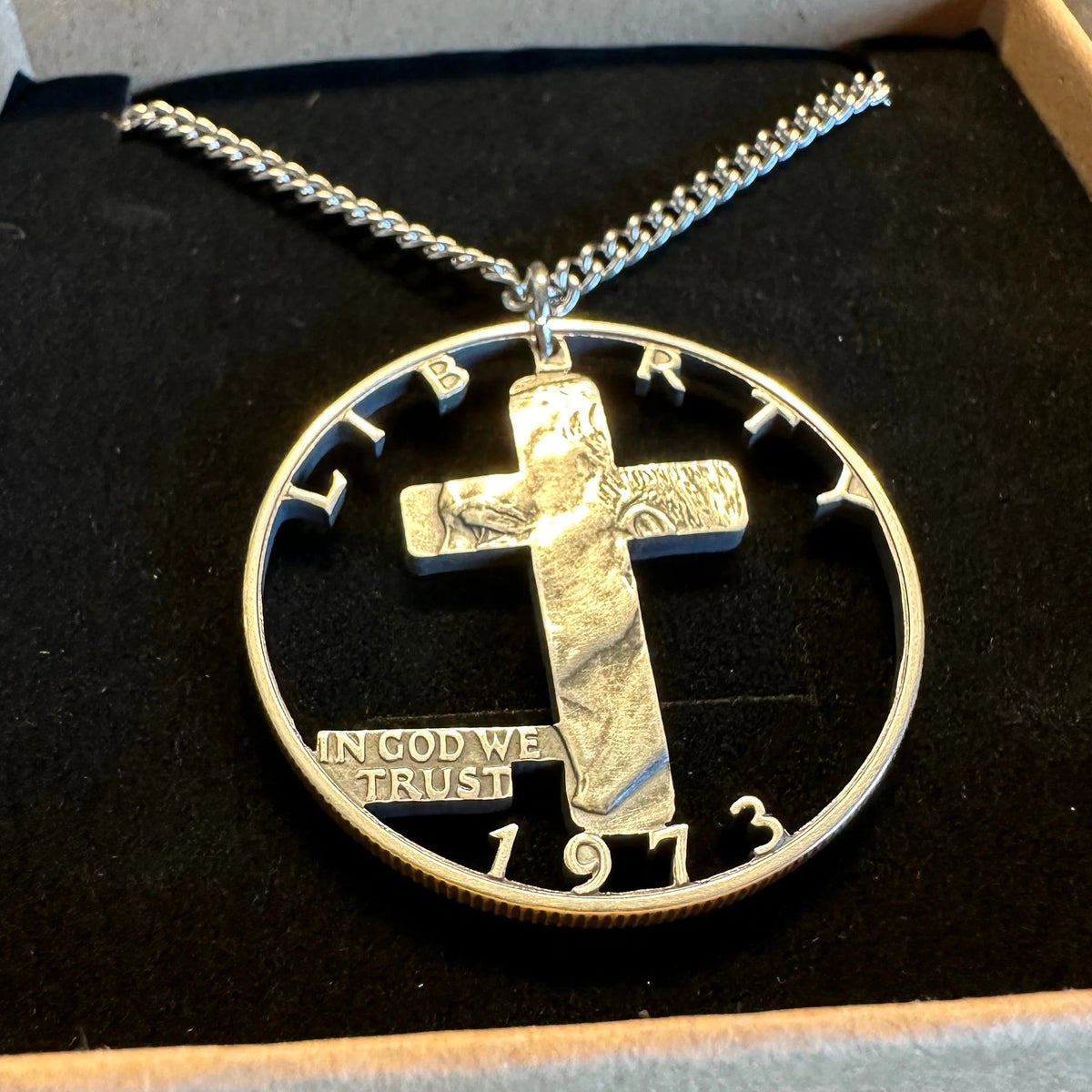 Silver Half Dollar coin necklace with a cross hand cut out on a black cushion in a box. -Mountainstruck Coin Jewelry