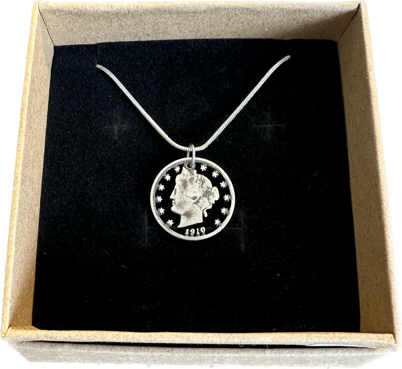 U.S. "V" Nickel Hand Cut Coin Necklace with a snake chain in a brown kraft box with a black velvet background.