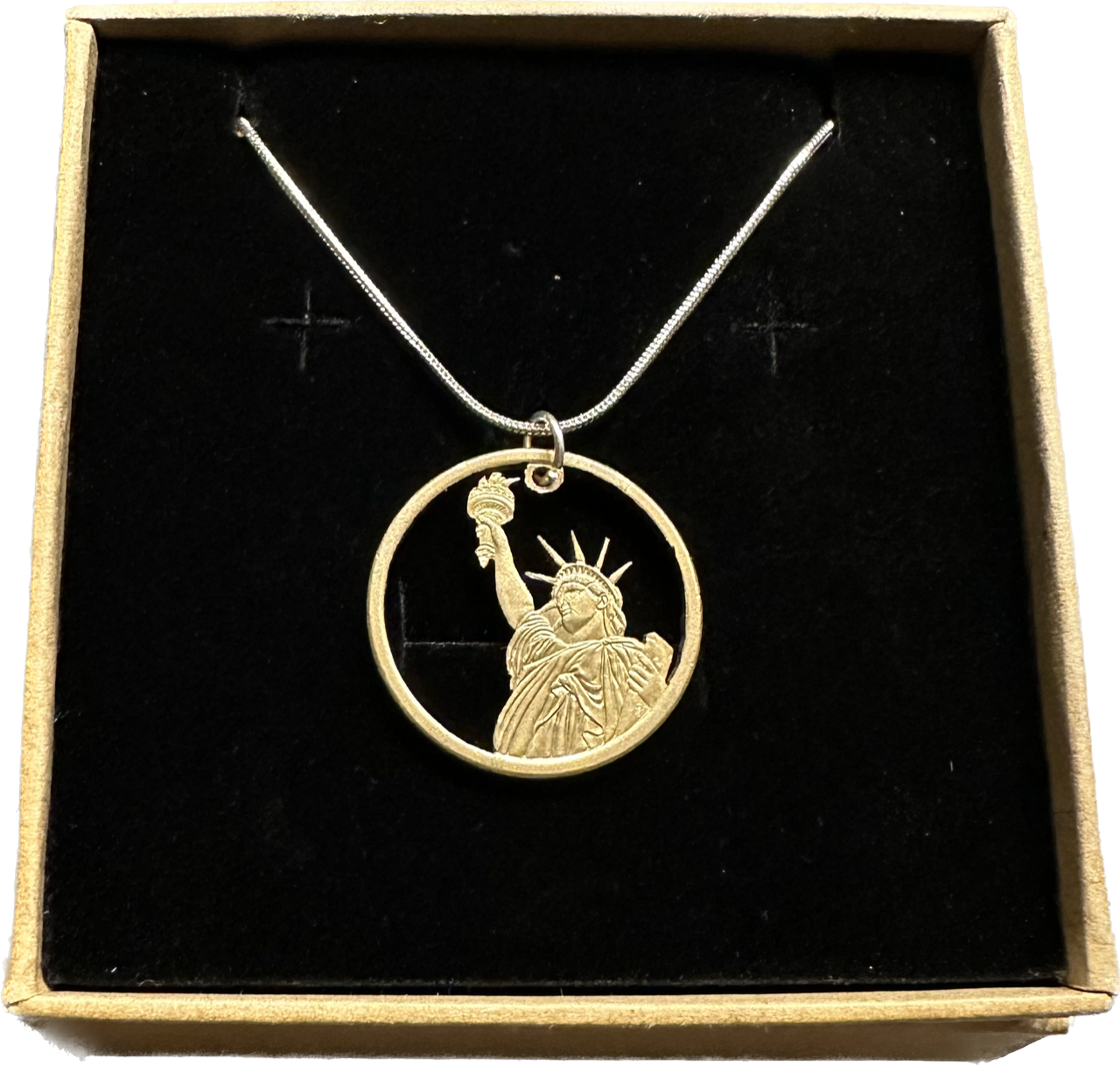 U.S. Statue of Liberty Gold Dollar Hand Cut Coin Necklace with a snake chain in a brown kraft box on a black velvet background.