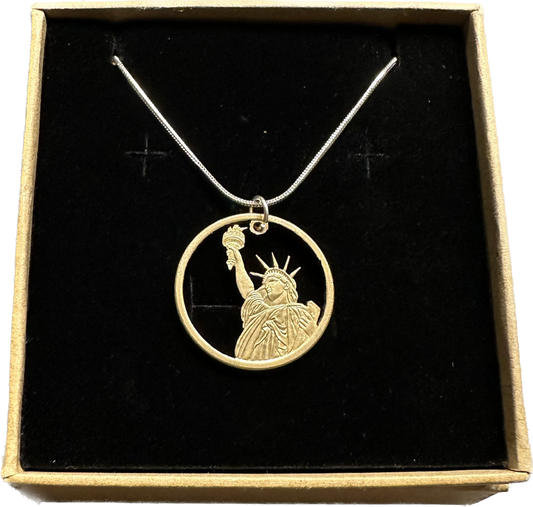 U.S. Statue of Liberty Gold Dollar Hand Cut Coin Necklace with a snake chain in a brown kraft box on a black velvet background.