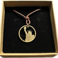 U.S. Statue of Liberty Gold Dollar Hand Cut Coin Necklace with leather cord in a brown kraft box on a black velvet background.