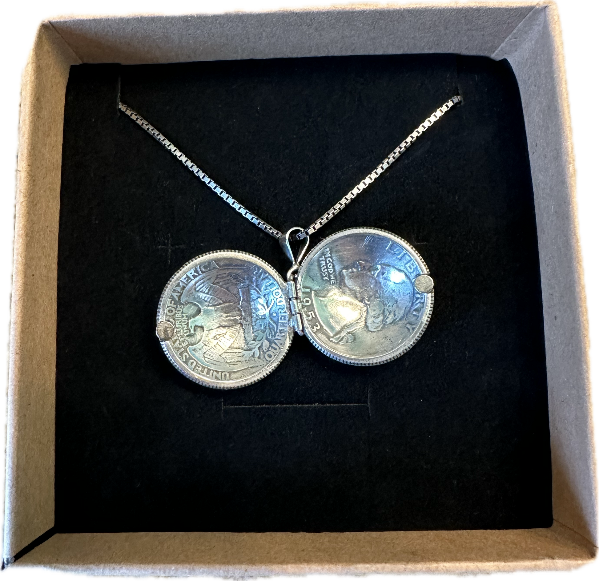 U.S. Silver Quarter Hand Crafted Coin Locket Necklace open in a brown kraft box on a black velvet background.