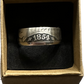 Seated Liberty Silver Half Dollar Coin Ring (patina) in a brown kraft box on a black velvet background.