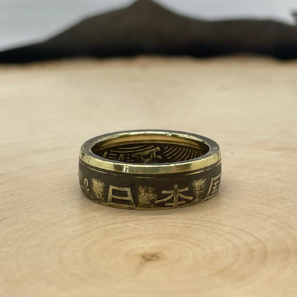 Japan 5 Yen Coin Ring on a light wood round with a mountain outline in the background. - Mountainstruck Coin Jewelry