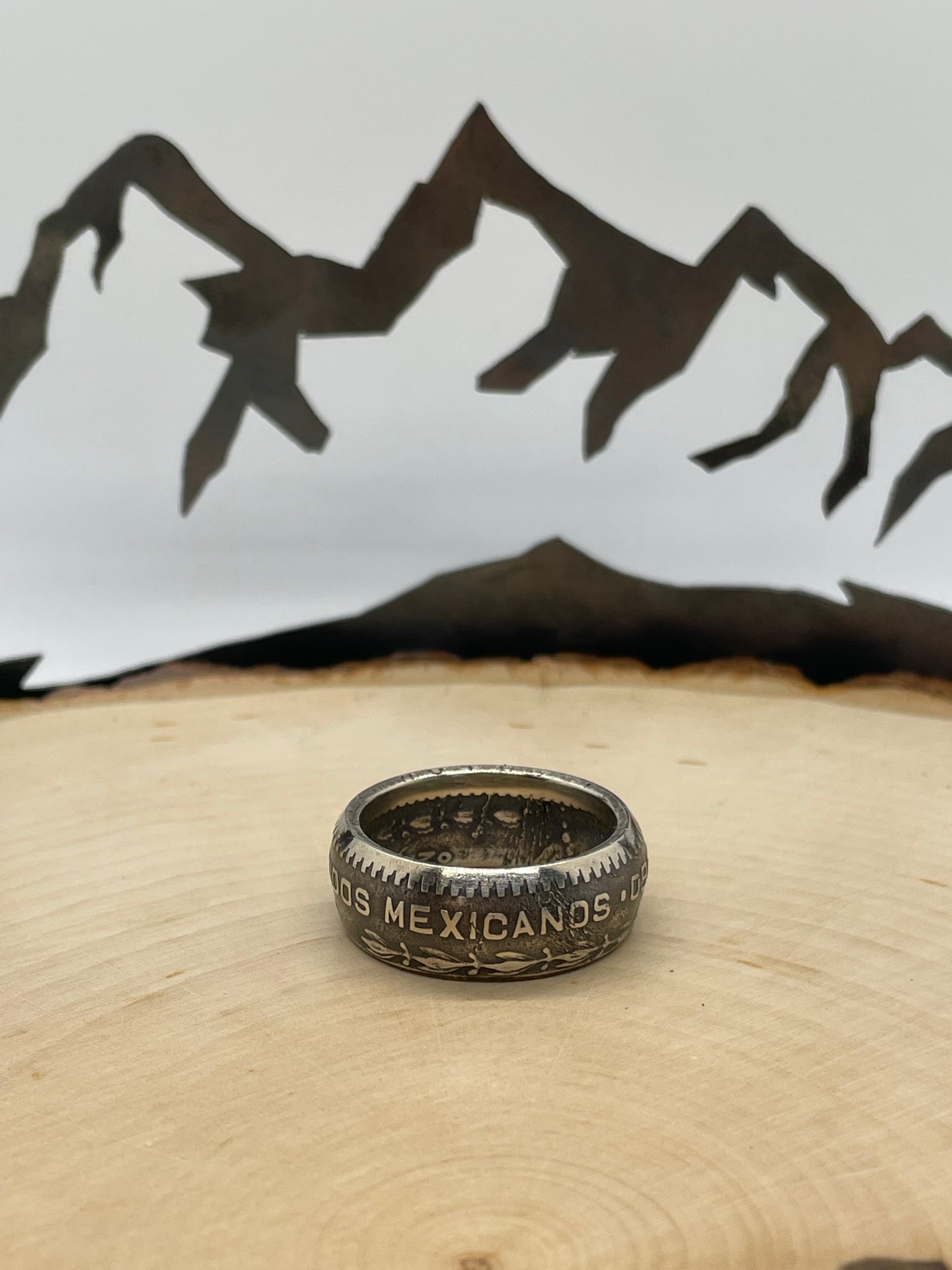 Mexico Silver Peso Coin Ring on a light wood round with mountain outline in the background. - Mountainstruck Coin Jewelry