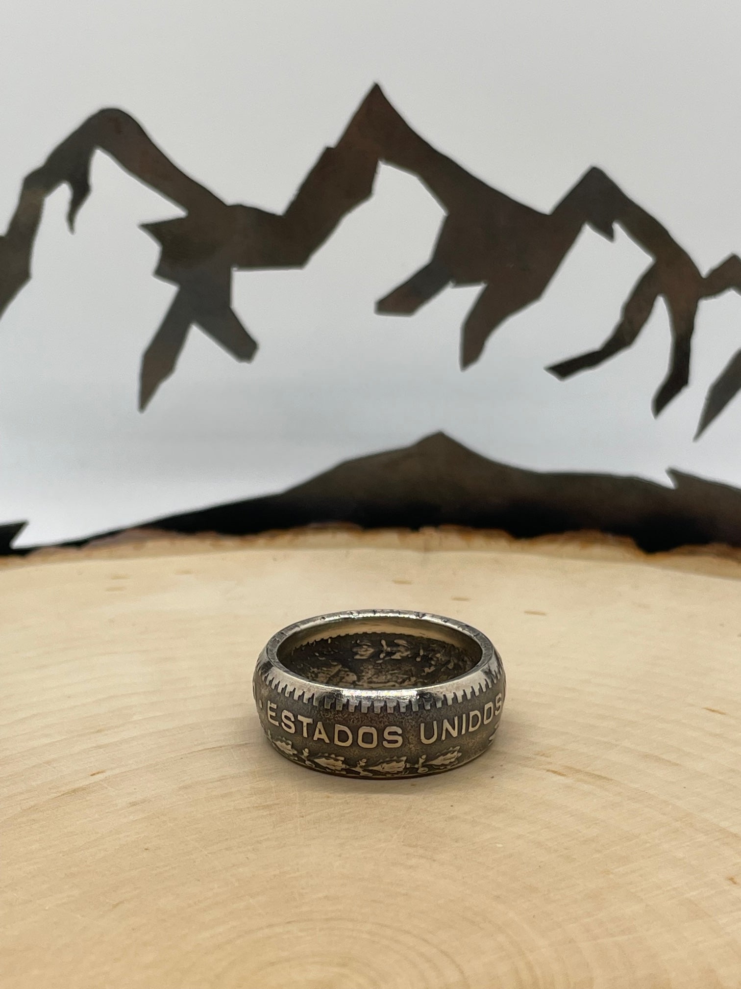 Mexico Silver Peso Coin Ring on a light wood round with mountain outline in the background. - Mountainstruck Coin Jewelry