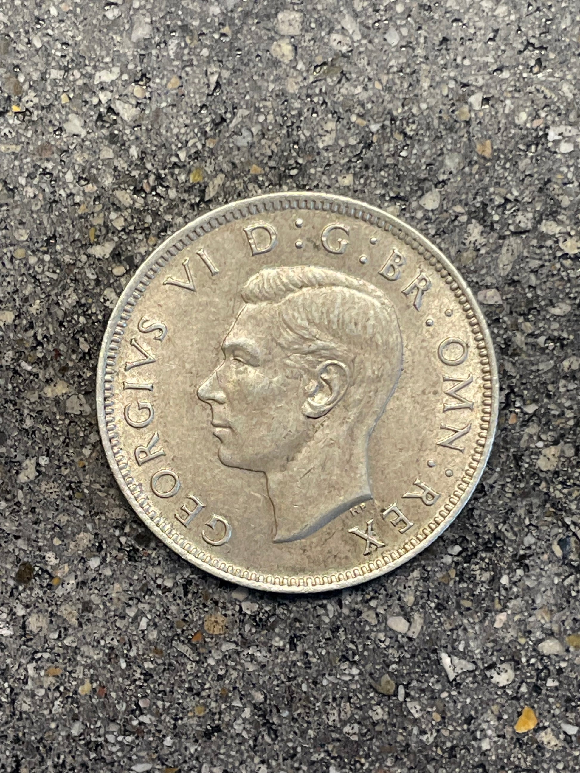 UK Two Shillings Silver Coin front on a concrete background.