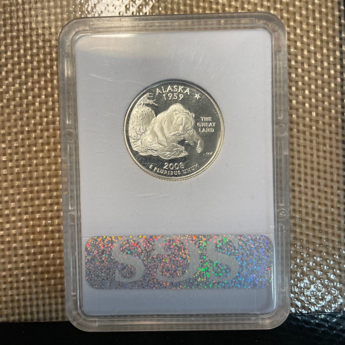 U.S. State Quarter Silver Coin Ring featuring Alaska in a plastic verification case on a woven background. - Mountainstruck Coin Jewelry