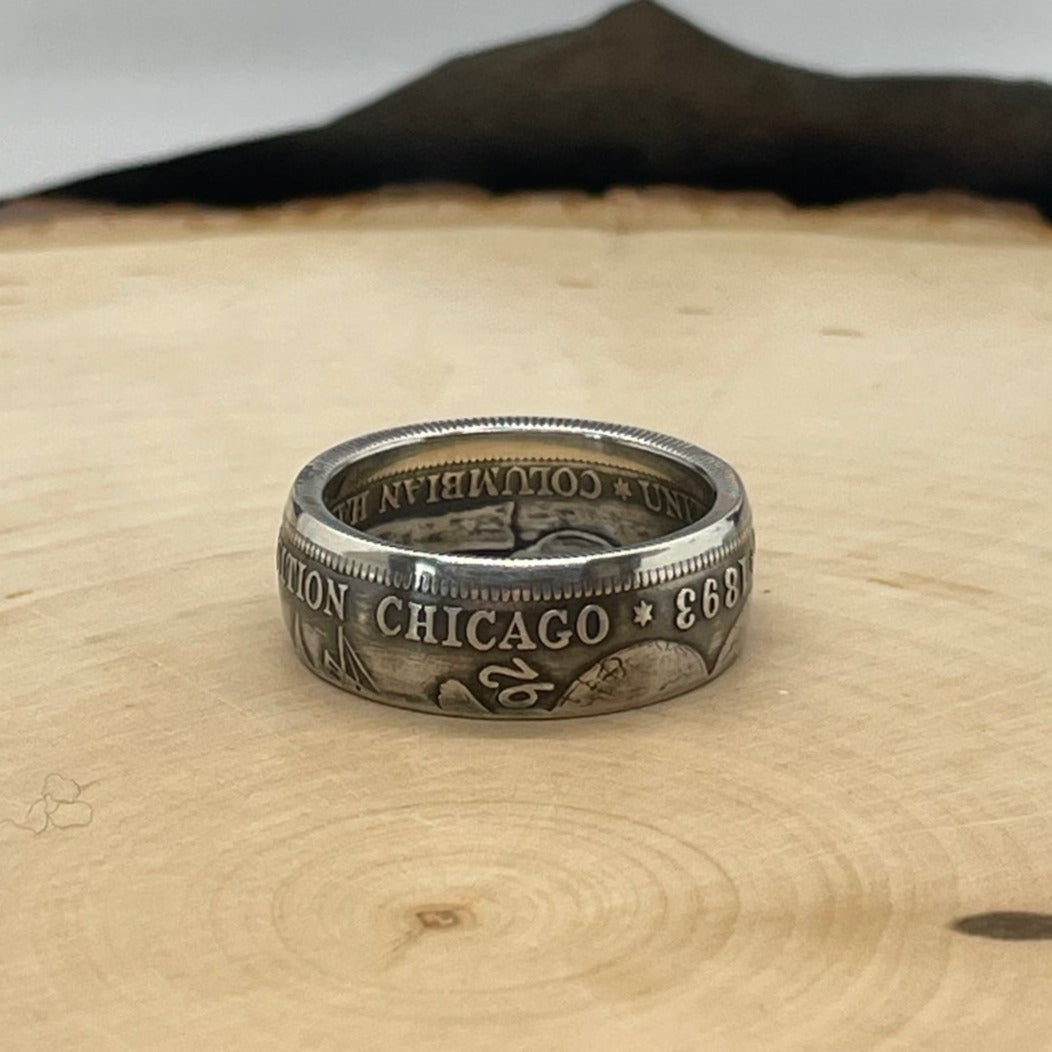  U.S. 1892-1893 Chicago Columbus Half Dollar Silver Coin Ring (patina) on a light wood round background. - Mountainstruck Coin Jewelry
