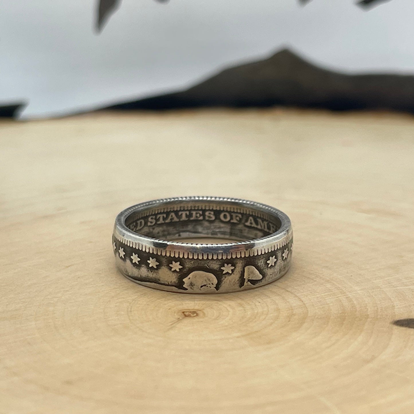 U.S. Seated Liberty Silver Quarter Coin Ring on a light wood round with mountain outline in the background. - Mountainstruck Coin Jewelry