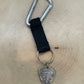 Guitar Pick U.S. Half Dollar Keychain with a black strap on a light wood round.