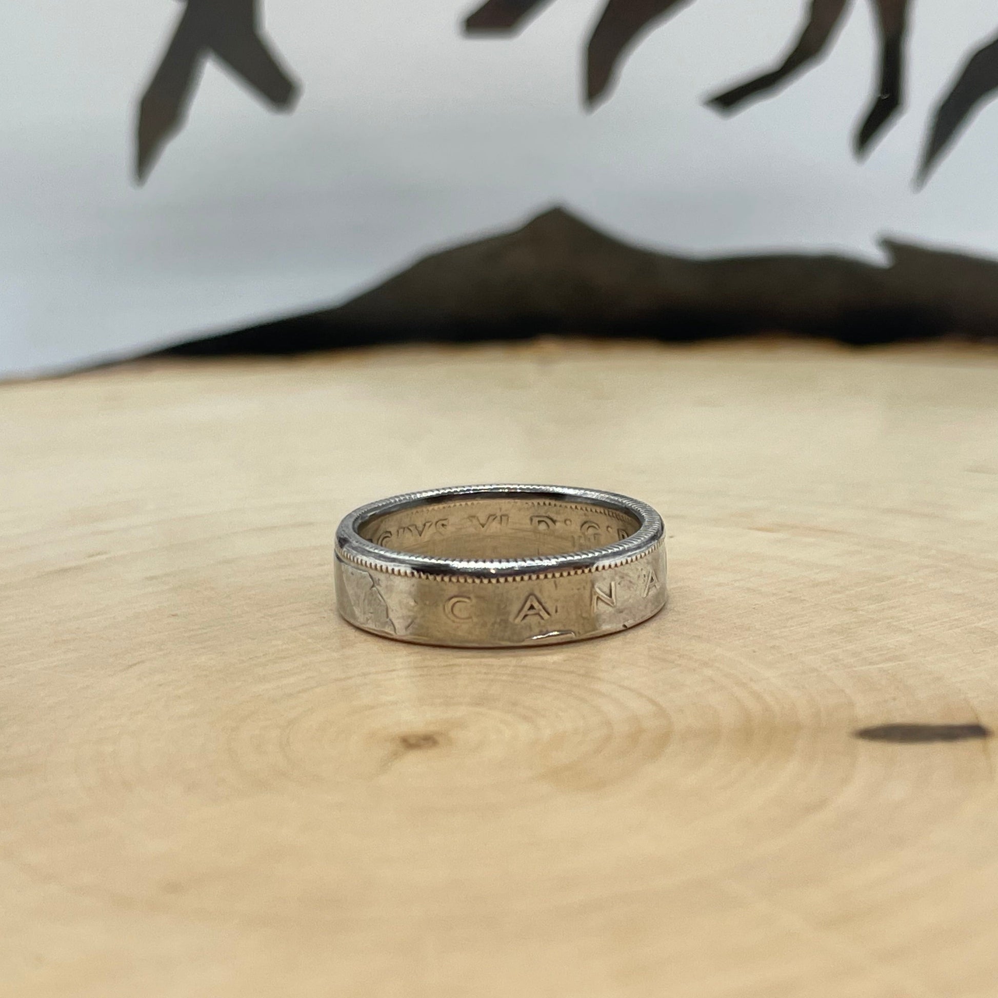 Canada 25 Cents Silver Coin Ring on a light wood round with a mountain outline background.