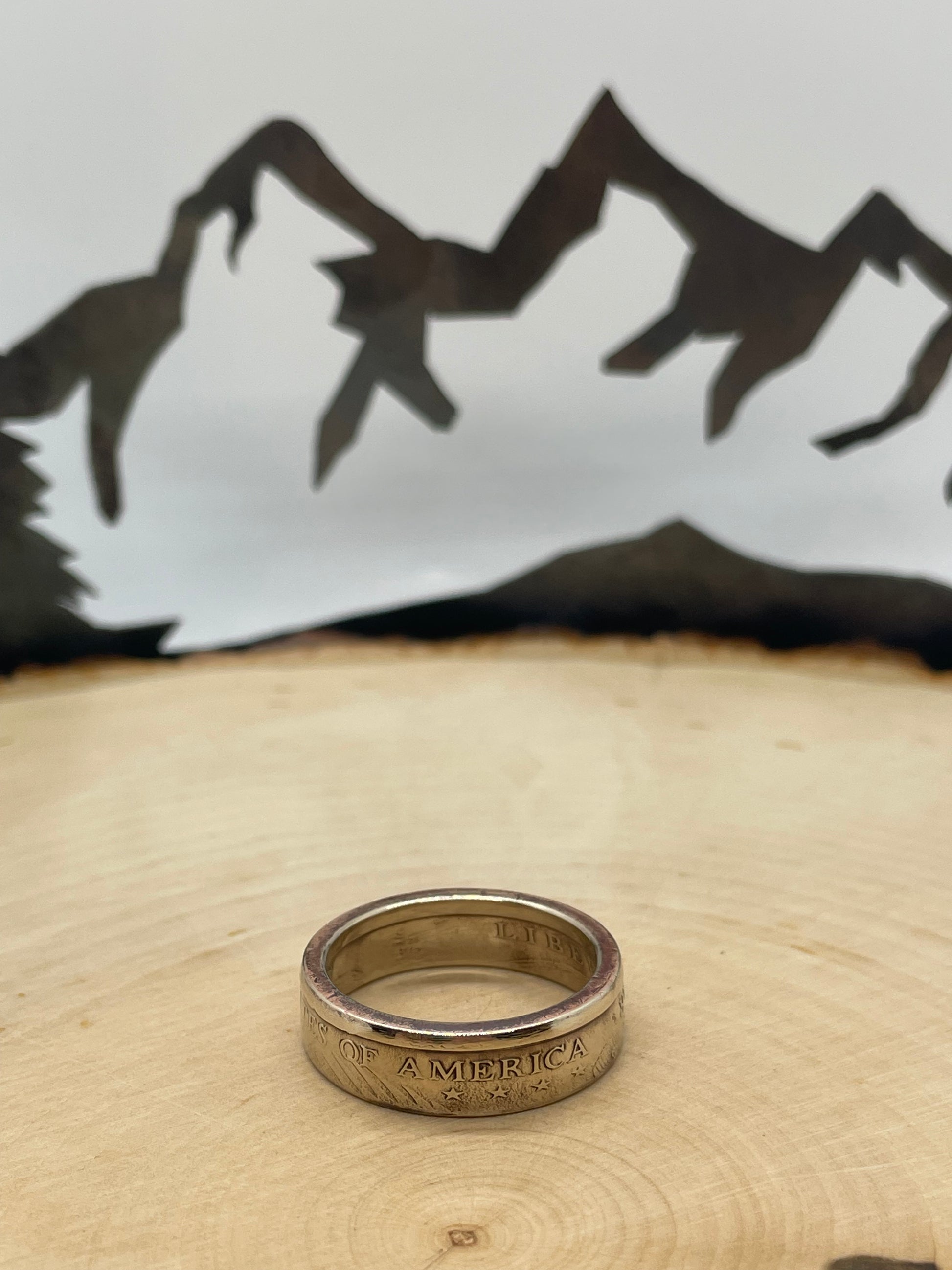 Sacagawea Dollar Coin Ring on a light wood round with mountain outline in background.