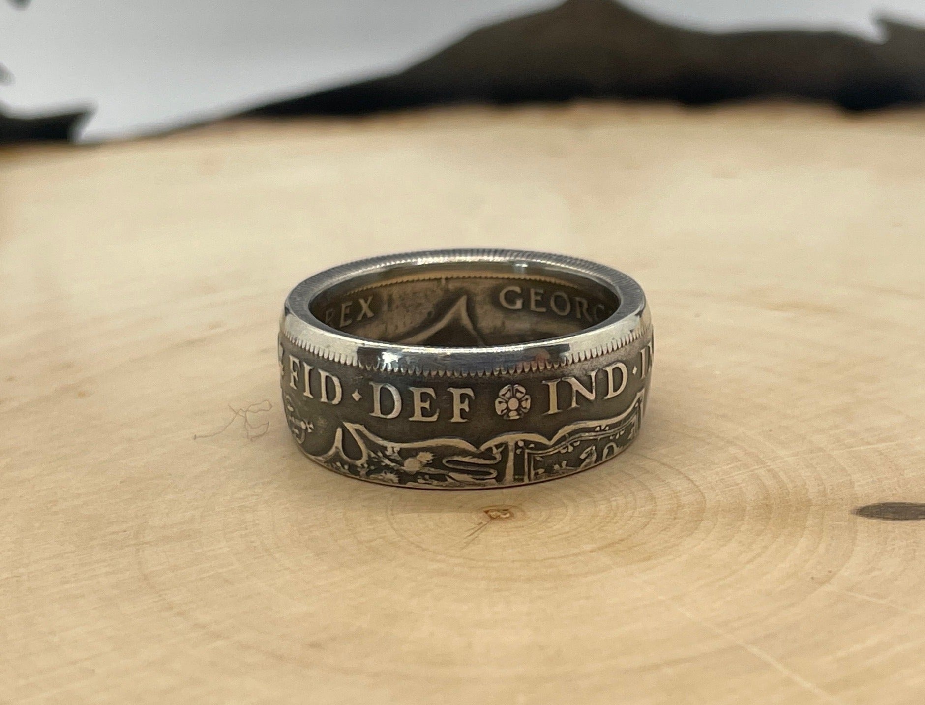 UK Half Crown Silver Coin Ring (1927-1936, G.B.) on a light wood round with mountain outline in background.